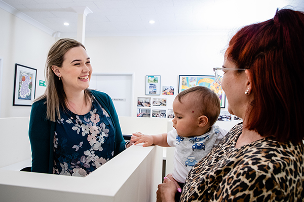 A woman behind a counter facing a mother with a baby